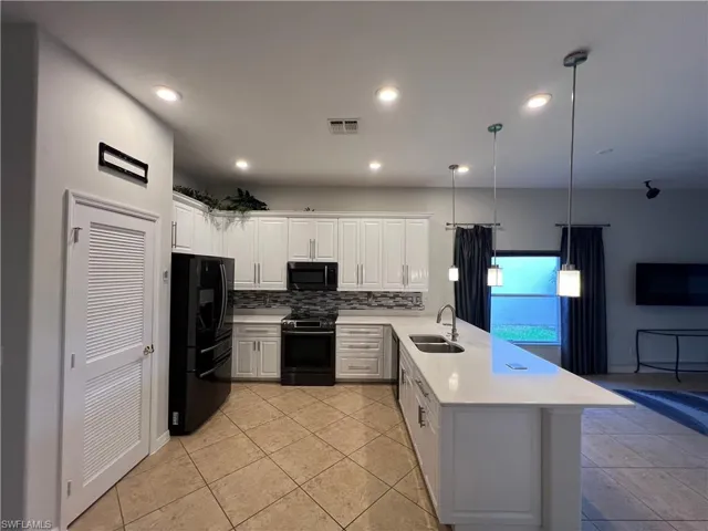 Kitchen with white cabinets, decorative backsplash, black appliances, decorative light fixtures, and a peninsula
