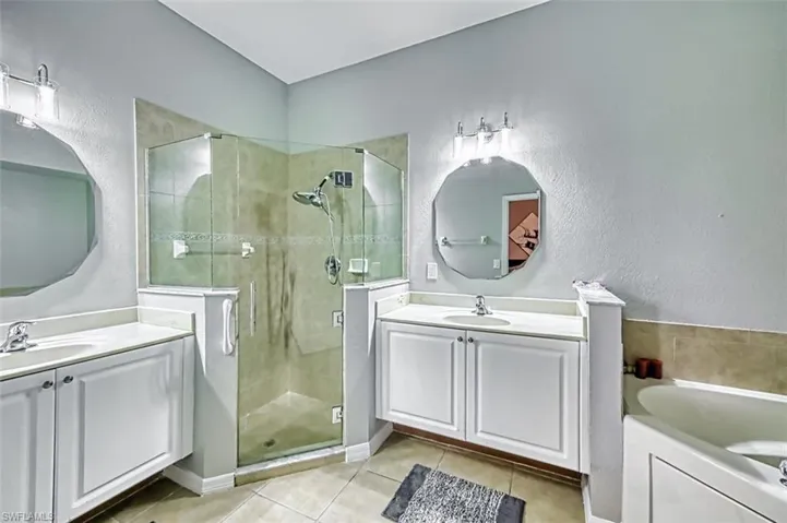 Bathroom featuring a stall shower, light tile patterned floors, two vanities, a bath, and a textured wall