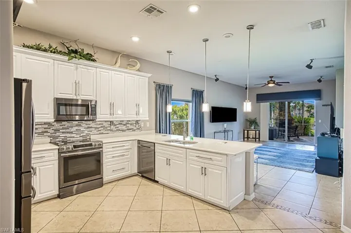 Kitchen with light tile patterned flooring, appliances with stainless steel finishes, white cabinets, hanging light fixtures, and recessed lighting
