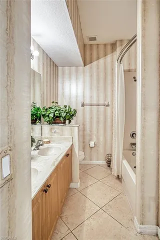 Bathroom featuring shower / bath combo, light tile patterned floors, and double vanity