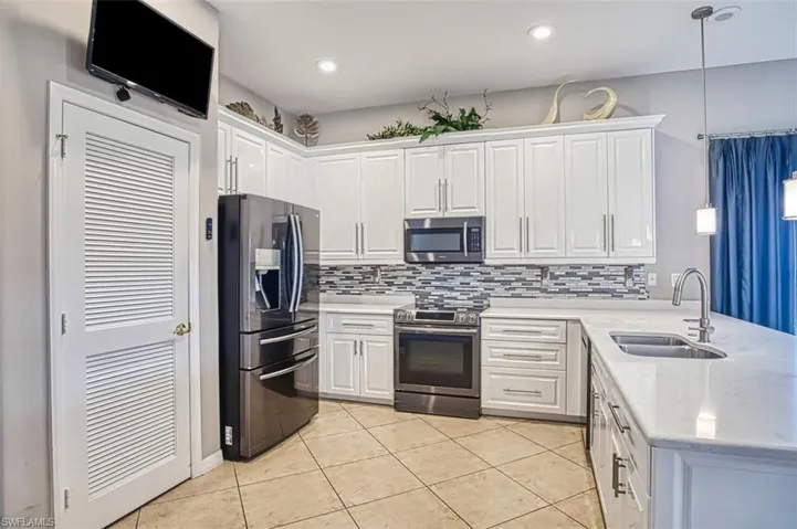 Kitchen featuring pendant lighting, appliances with stainless steel finishes, a peninsula, white cabinetry, and light stone counters