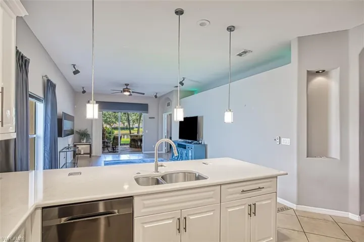 Kitchen featuring dishwasher, light tile patterned floors, hanging light fixtures, and white cabinetry