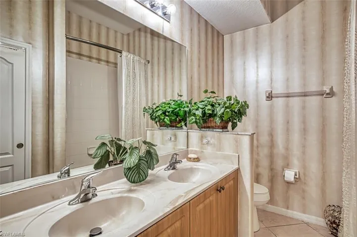 Full bath featuring double vanity, light tile patterned floors, and curtained shower