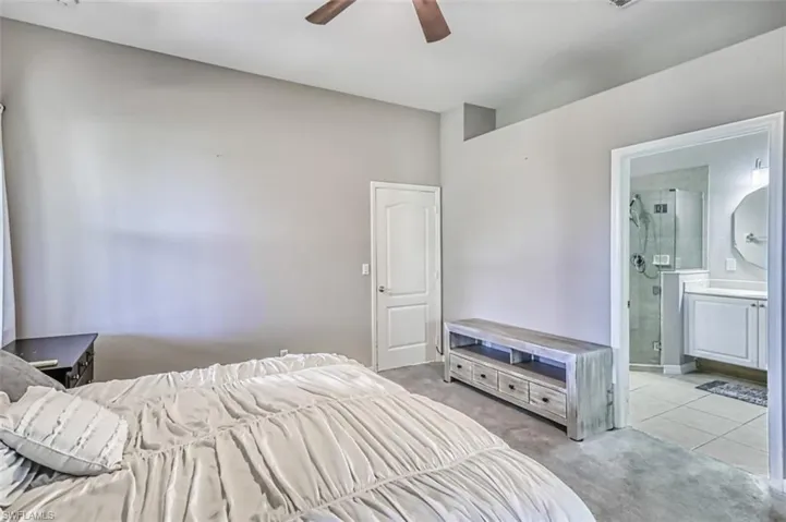 Bedroom with light colored carpet, a ceiling fan, ensuite bath, and light tile patterned floors