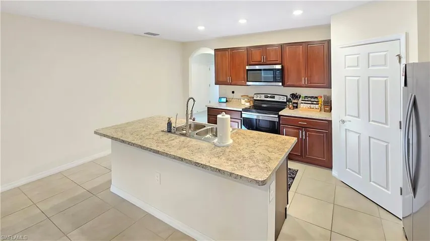 Kitchen featuring arched walkways, stainless steel appliances, a sink, visible vents, and an island with sink
