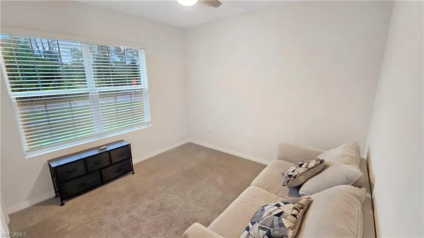 Living area featuring light carpet, baseboards, and a ceiling fan