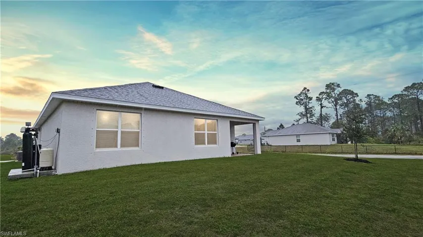 Back of house at dusk with roof with shingles, fence, a lawn, and stucco siding