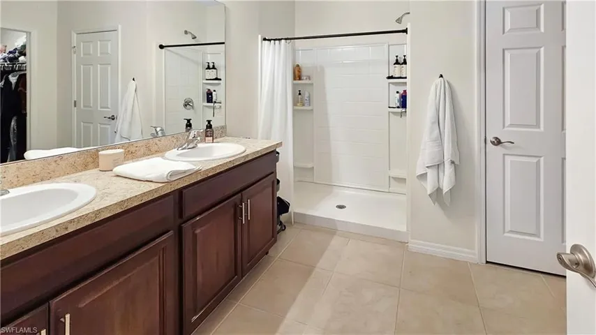 Full bathroom with a stall shower, a walk in closet, a sink, and tile patterned floors
