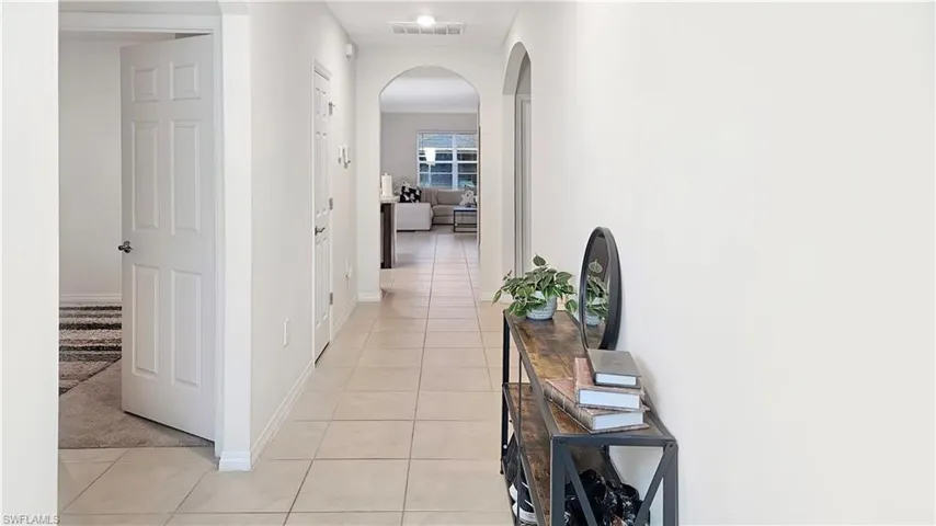 Hall featuring arched walkways, visible vents, baseboards, and light tile patterned flooring
