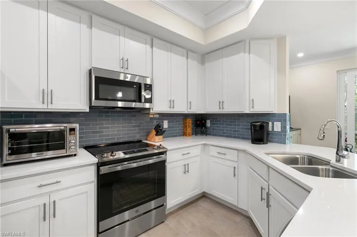 Kitchen featuring a toaster, light countertops, decorative backsplash, stainless steel appliances, and a sink