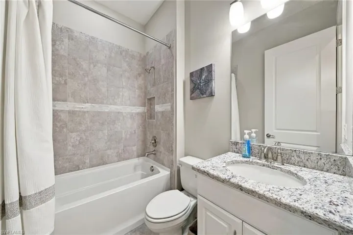 Bathroom featuring a stone-pattern vanity countertop with an undermount oval sink, a tiled bathtub surround with an inset niche, a large wall-mounted mirror, and overhead vanity lighting