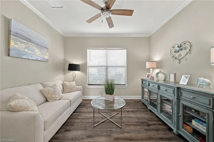 Wood-finish flooring, crown molding, and a central ceiling fan with integrated lighting