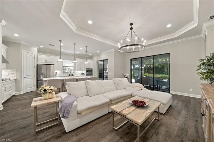 Tray ceiling with recessed lighting, wood-finish flooring, island kitchen with pendant lighting, and multi-panel sliding glass doors