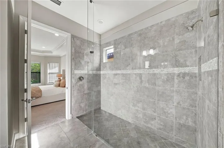 Walk-in shower featuring large-format tile wall surround, glass enclosure, mosaic tile accent border, and a fixed shower head