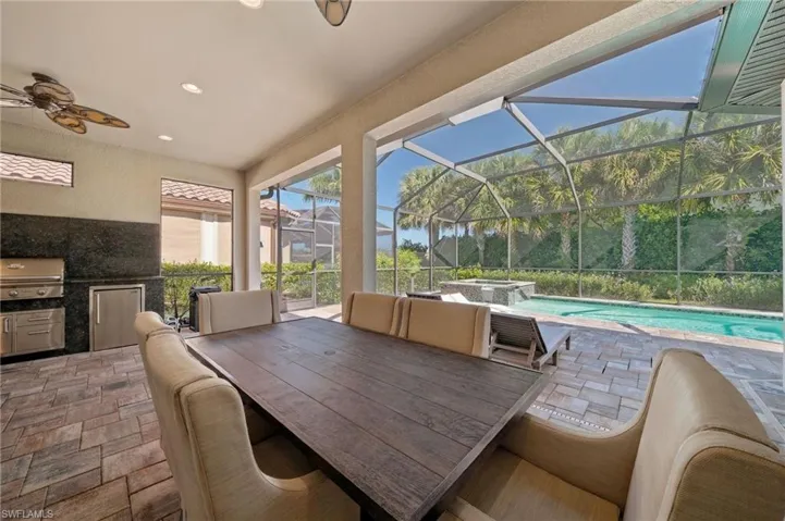 Covered patio featuring an outdoor kitchen with stainless steel appliances, stone-paver flooring, a screened enclosure, and an in-ground pool with a built-in spa