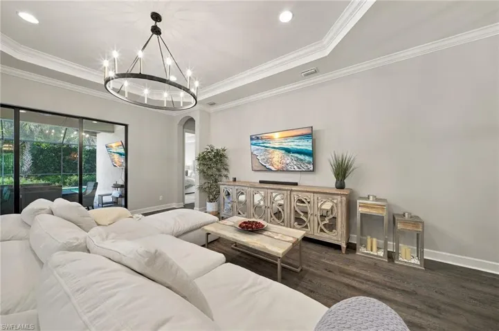 Living area featuring a tray ceiling with crown molding, wood-finish flooring, recessed lighting, a statement chandelier, and floor-to-ceiling sliding glass doors