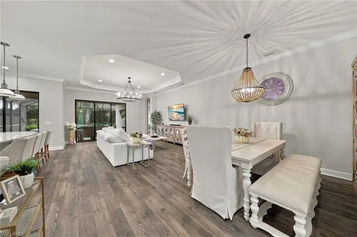 Open-concept floor plan featuring wood-finish flooring, a tray ceiling, dual chandeliers, and sliding glass doors