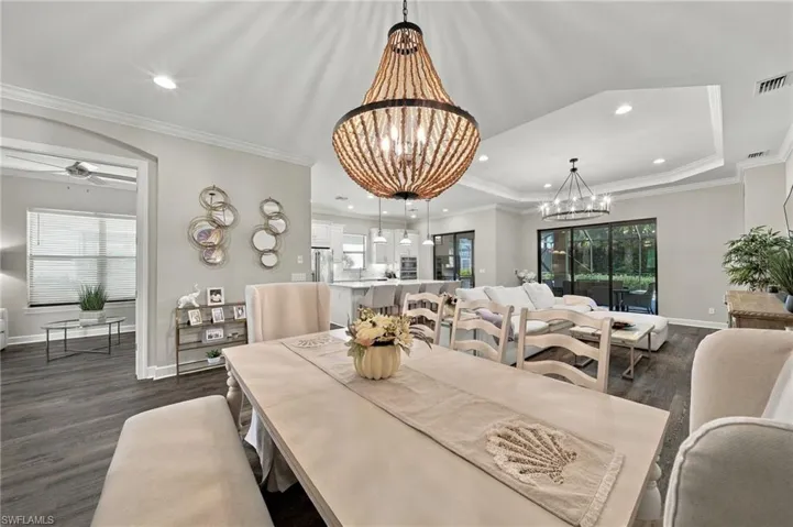 Open-concept interior featuring tray ceilings, wood-finish flooring, decorative beaded chandelier, and sliding glass doors