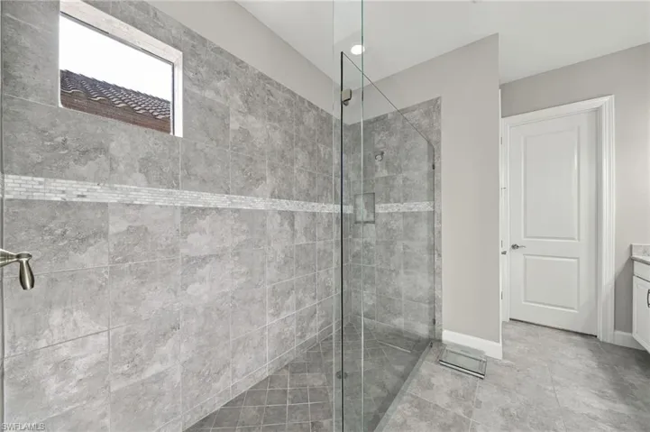 Walk-in shower featuring gray stone-finish wall tiles with a decorative accent strip, a frameless glass enclosure, a built-in recessed niche, and a transom window