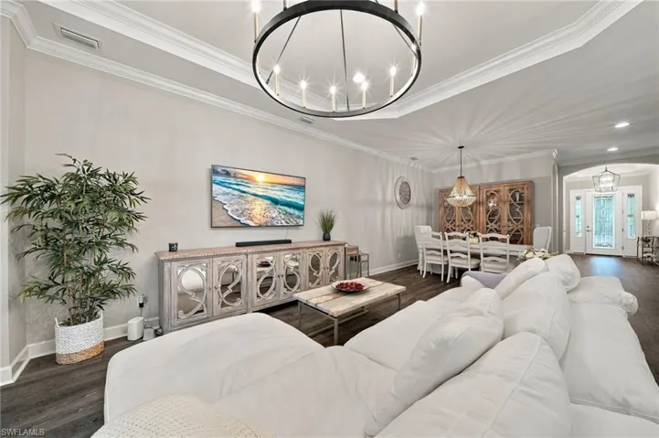 Tray ceiling with crown molding, dark wood-finish flooring, and industrial-style circular chandelier