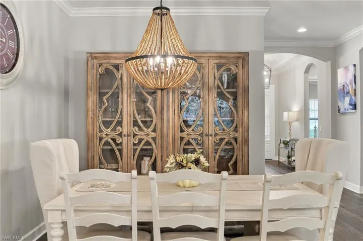 Dining space featuring built-in wooden cabinetry with glass-paneled doors, bead-detail chandelier, crown molding, and dark-finish flooring