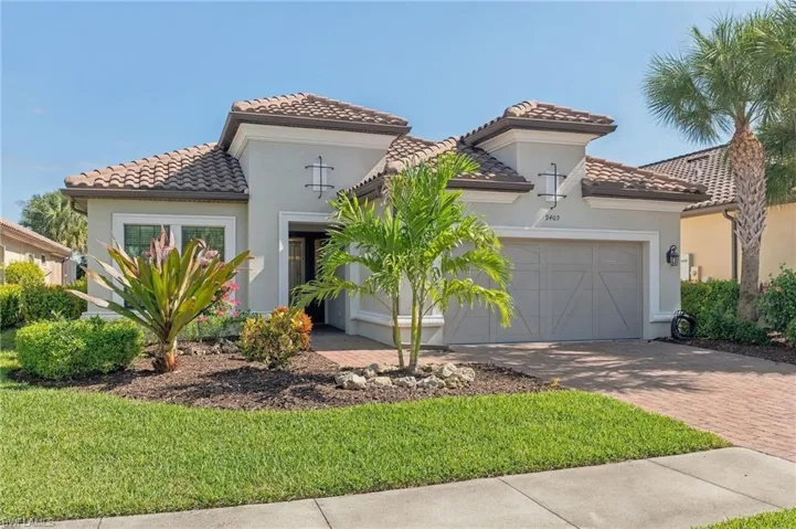 Stucco exterior residence featuring a tiled hip roof, brick-paver driveway, double-car carriage-style garage door, and integrated wall-mounted exterior lighting