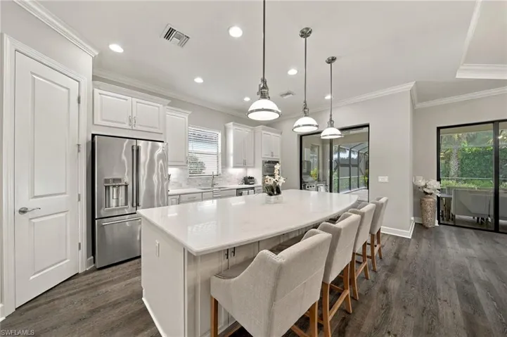 Kitchen featuring a large central island with light-toned stone-surface countertops, white cabinetry, stainless steel appliances, and three glass-shade pendant lights over wood-finish flooring