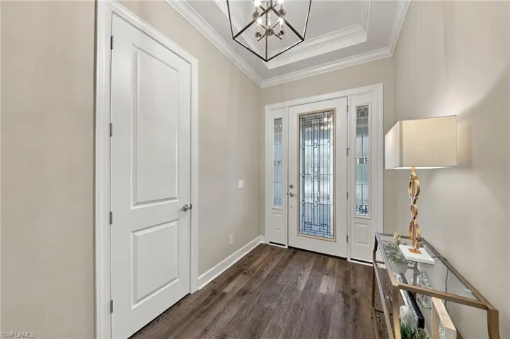 Entryway featuring wood-finish flooring, tray ceiling, geometric pendant lighting, and a front door with decorative glass paneling and matching sidelights
