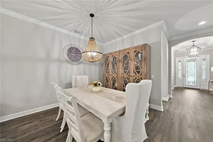 Dining area featuring wood-finish flooring, crown molding, a beaded chandelier, and built-in wood cabinetry with glass-paneled doors