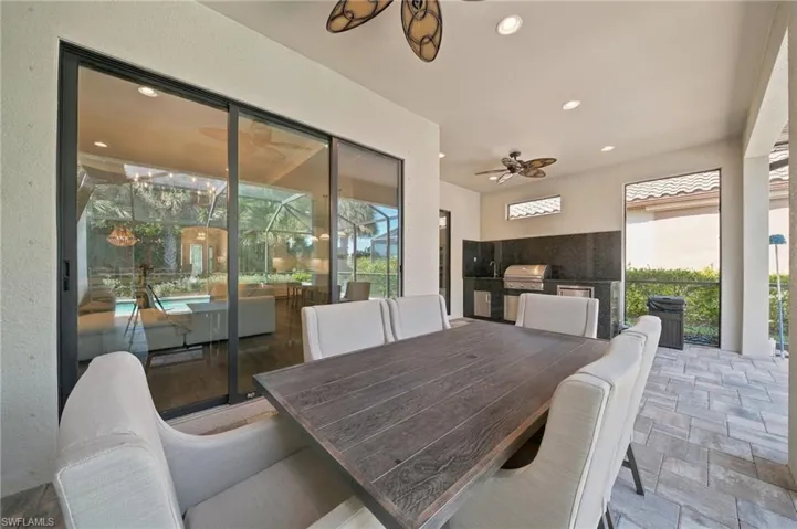 Covered outdoor patio featuring paver flooring, recessed lighting, ceiling fans, and an outdoor kitchen equipped with a stone-finish countertop and backsplash