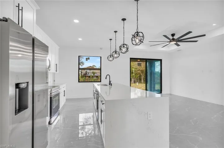 Kitchen with pendant lighting, sink, white cabinetry, stainless steel appliances, and light stone countertops