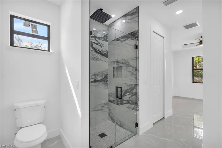 Bathroom featuring ceiling fan, toilet, and an enclosed shower