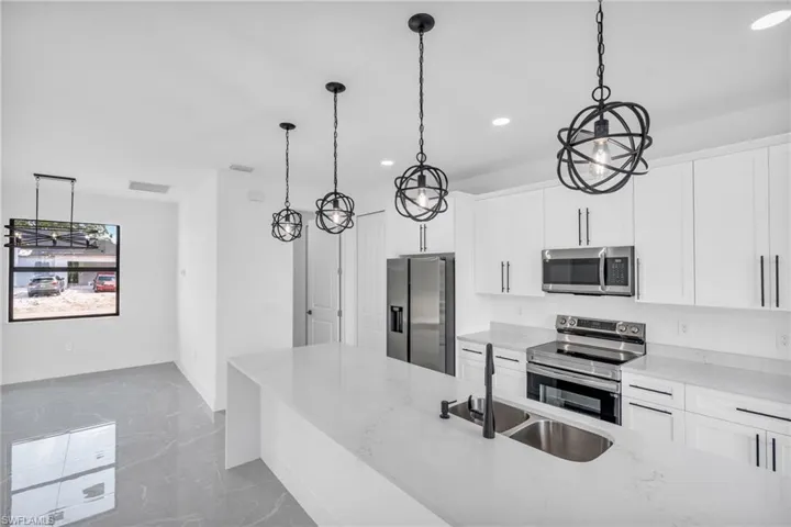 Kitchen featuring pendant lighting, sink, appliances with stainless steel finishes, white cabinetry, and an island with sink
