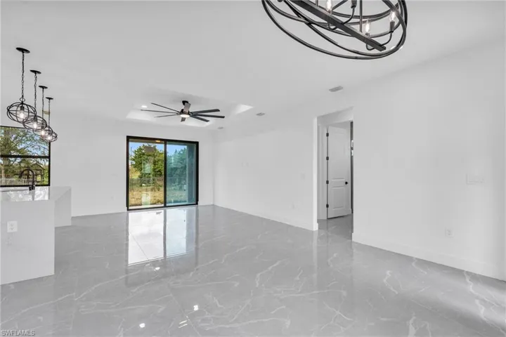 Kitchen featuring sink, white cabinetry, stainless steel appliances, an island with sink, and decorative light fixtures