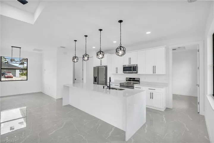 Kitchen with white cabinetry, a center island with sink, a raised ceiling, pendant lighting, and stainless steel appliances