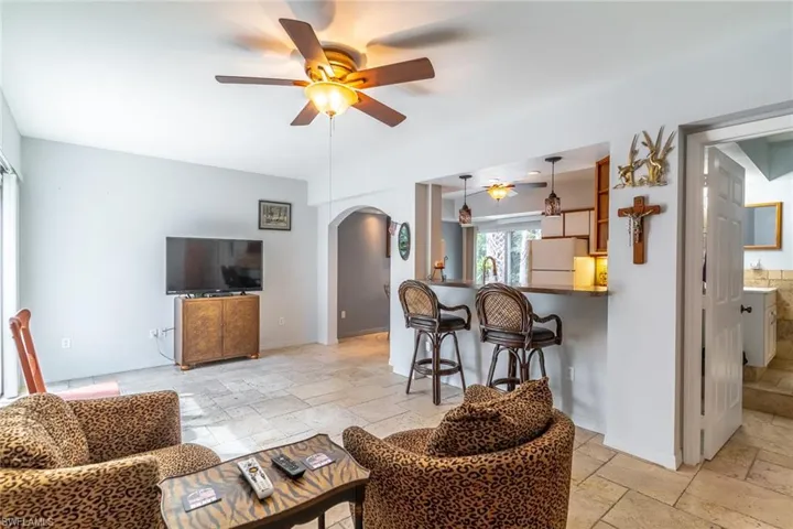 Living room with stone tile flooring, a ceiling fan, and arched feature