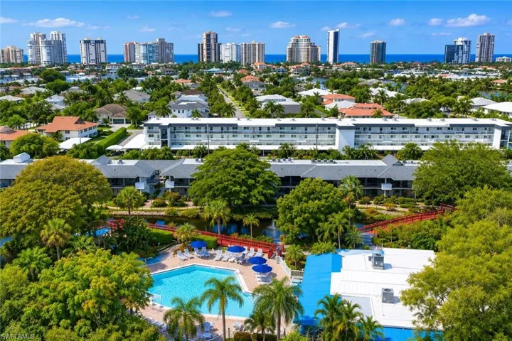 Expansive community featuring a large swimming pool with surrounding lounge chairs and blue umbrellas, surrounded by lush tropical landscaping