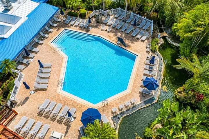 Resort-style pool area featuring a large, geometric swimming pool with integrated steps, surrounded by extensive paver decking