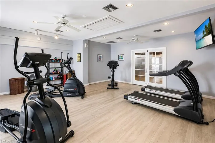 Fitness room with wood-finish flooring, two ceiling fans, recessed lighting, and double French doors with frosted glass panels