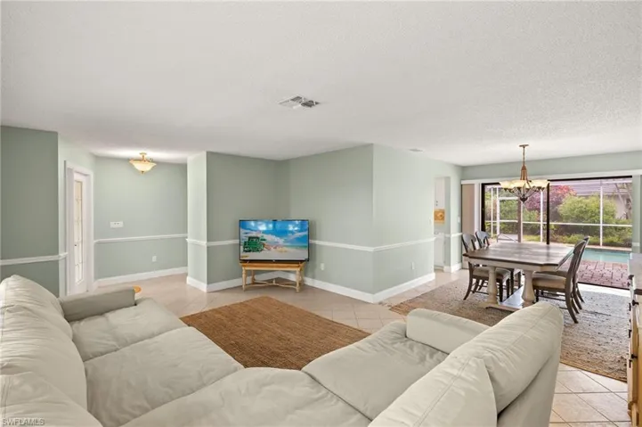 Living room featuring a chandelier, a textured ceiling, light tile patterned floors, and baseboards
