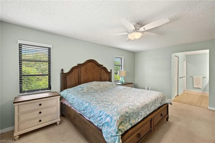 Bedroom featuring light colored carpet, a textured ceiling, baseboards, ceiling fan, and light tile patterned floors