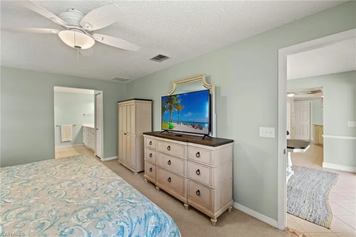 Bedroom featuring light tile patterned floors, baseboards, ensuite bath, a textured ceiling, and ceiling fan