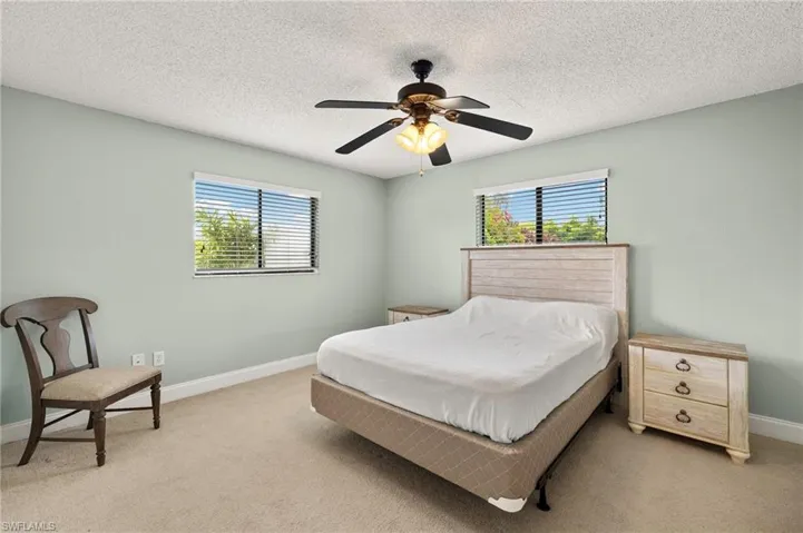 Bedroom with multiple windows, baseboards, light colored carpet, ceiling fan, and a textured ceiling