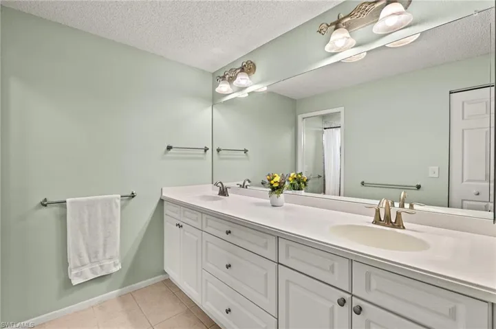 Full bath with double vanity, tile patterned floors, a textured ceiling, and baseboards