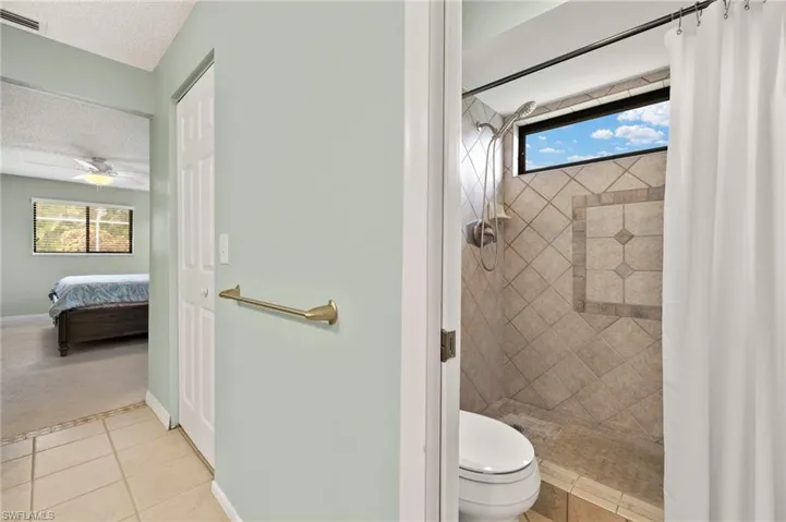 Ensuite bathroom featuring a textured ceiling, a tile shower, toilet, tile patterned floors, and ceiling fan