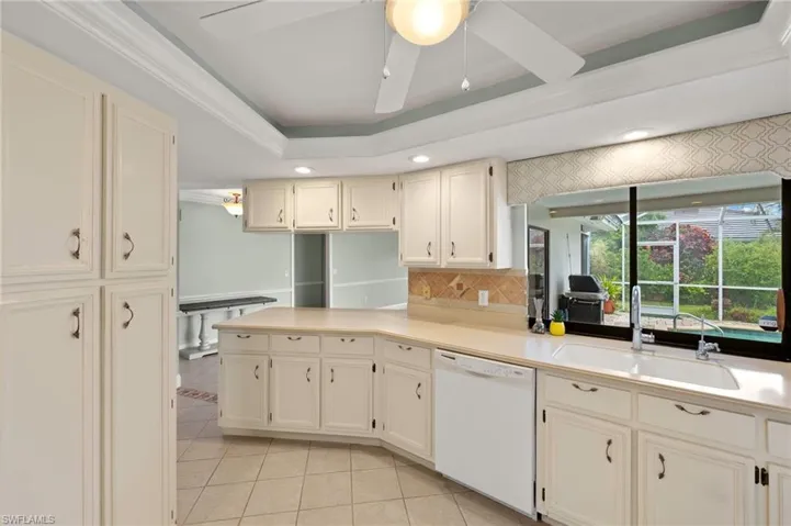 Kitchen with white dishwasher, a sink, light tile patterned floors, decorative backsplash, and light countertops