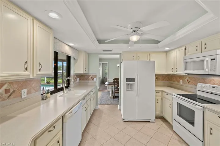 Kitchen featuring white appliances, cream cabinetry, a sink, a raised ceiling, and light countertops