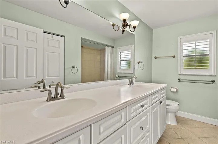 Full bathroom featuring toilet, tile patterned flooring, double vanity, baseboards, and a shower with shower curtain