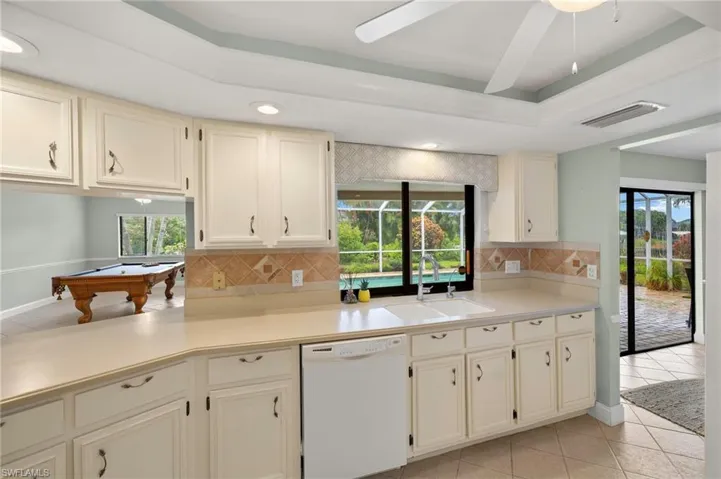 Kitchen featuring white dishwasher, a sink, backsplash, light tile patterned floors, and billiards table