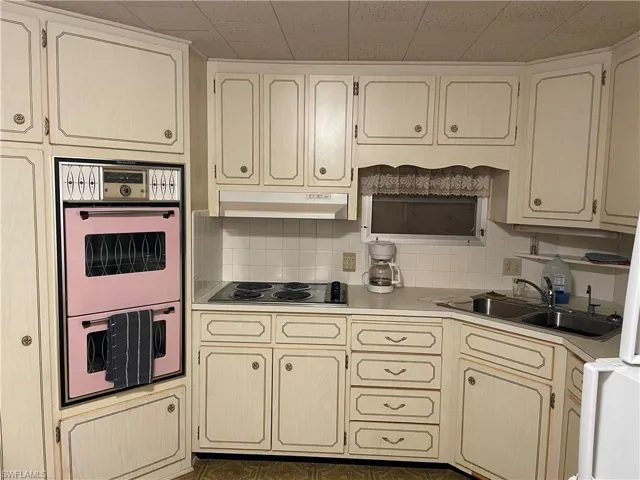 Kitchen with black electric stovetop, cream cabinetry, sink, tasteful backsplash, and multiple ovens